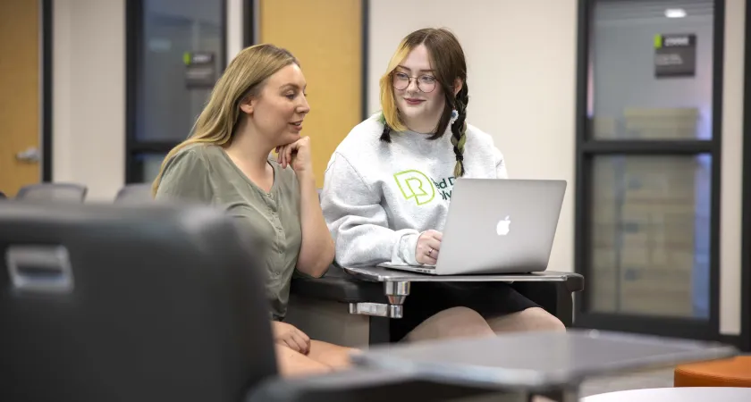 Two women sitting together with an open laptop.