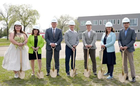 A group of RDP and Government of Alberta reps wear hardhats while holding shovels