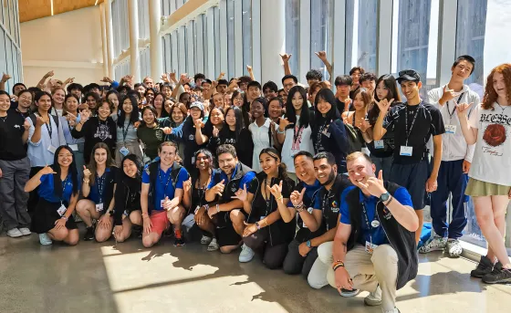 A large group of diverse high school students pose in a long corridor of windows