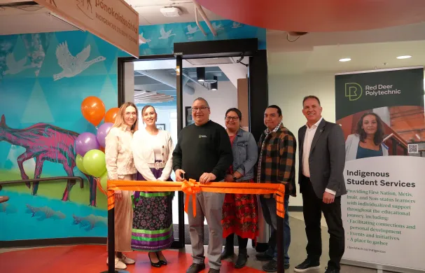 A group of RDP staff and students stand in front of an orange ribbon ready to cut it