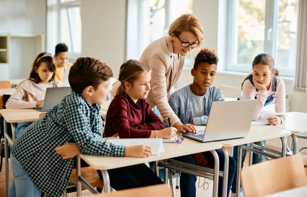 A group of youth learn with a teacher pointing to a laptop