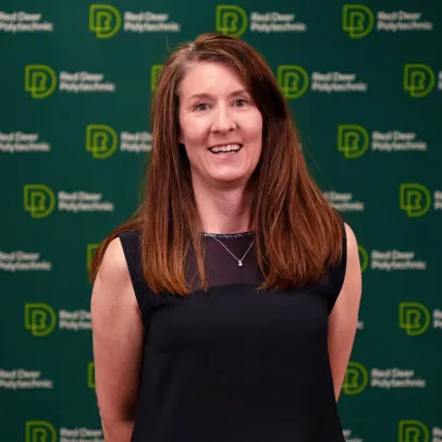 Karen Walkley has long brown hair, wears a black sleeveless shirt and smiles in front of an RDP backdrop