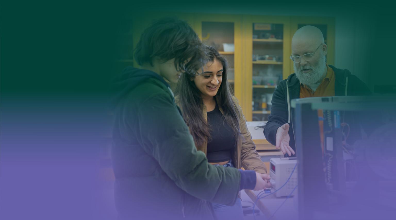 Two students look at a piece of tech in a lab as an instructor explains how to use it