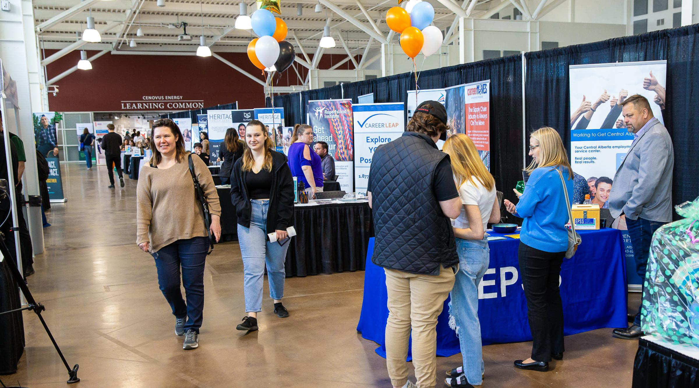 Employer booths line the right side of the photo, small groups of people talking in the booths and two attendees are walking towards the camera.