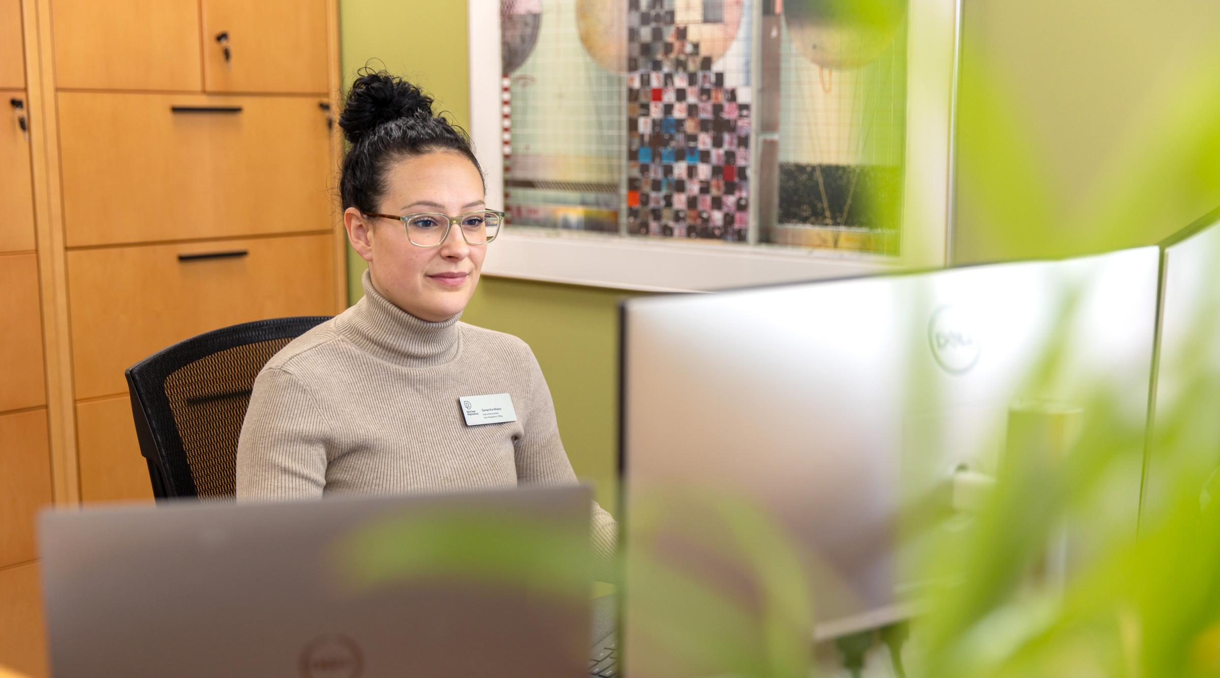 An executive assistant works at a desk with artwork & green plants surrounding her.
