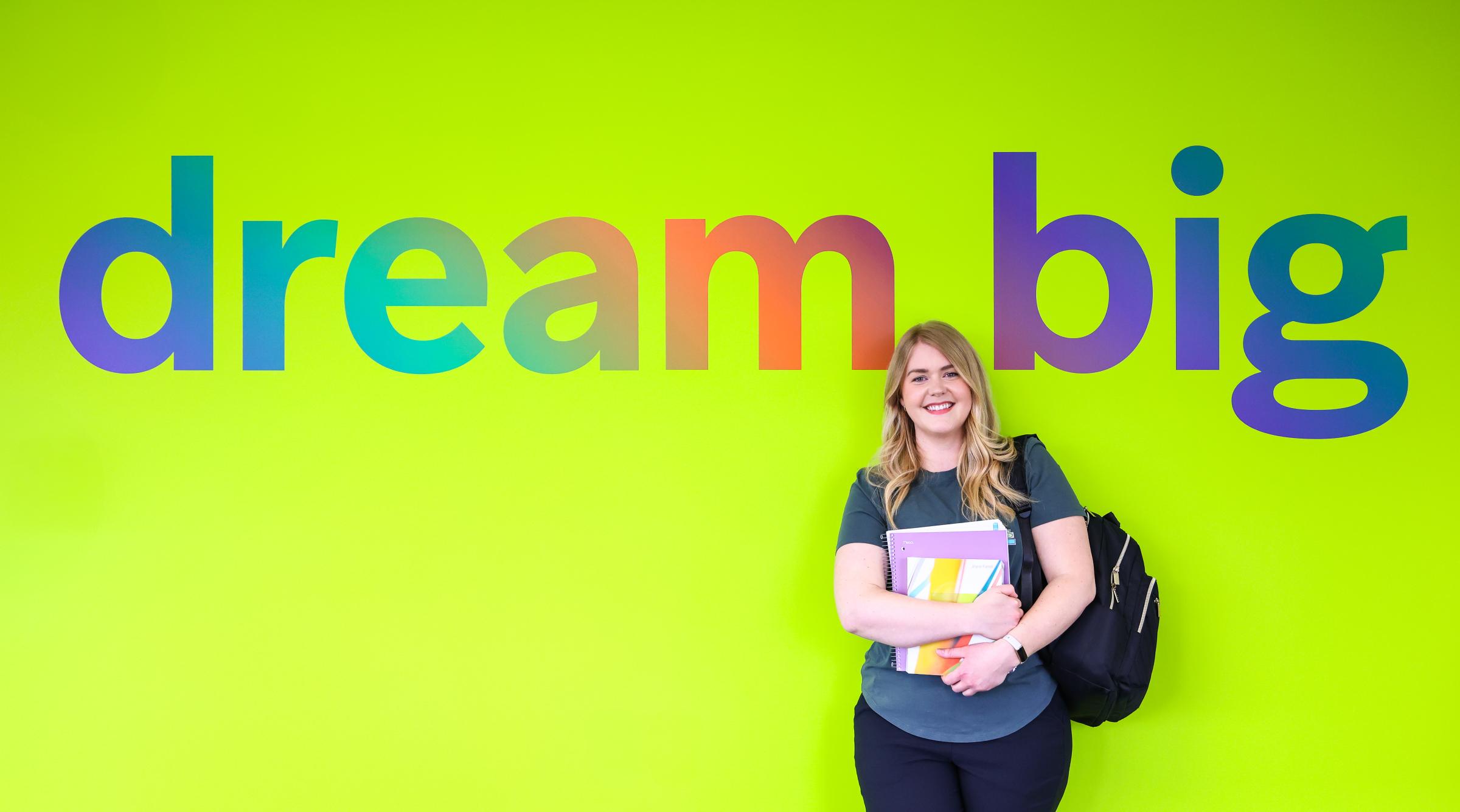 Mature student against a green wall stating "Dream Big,"