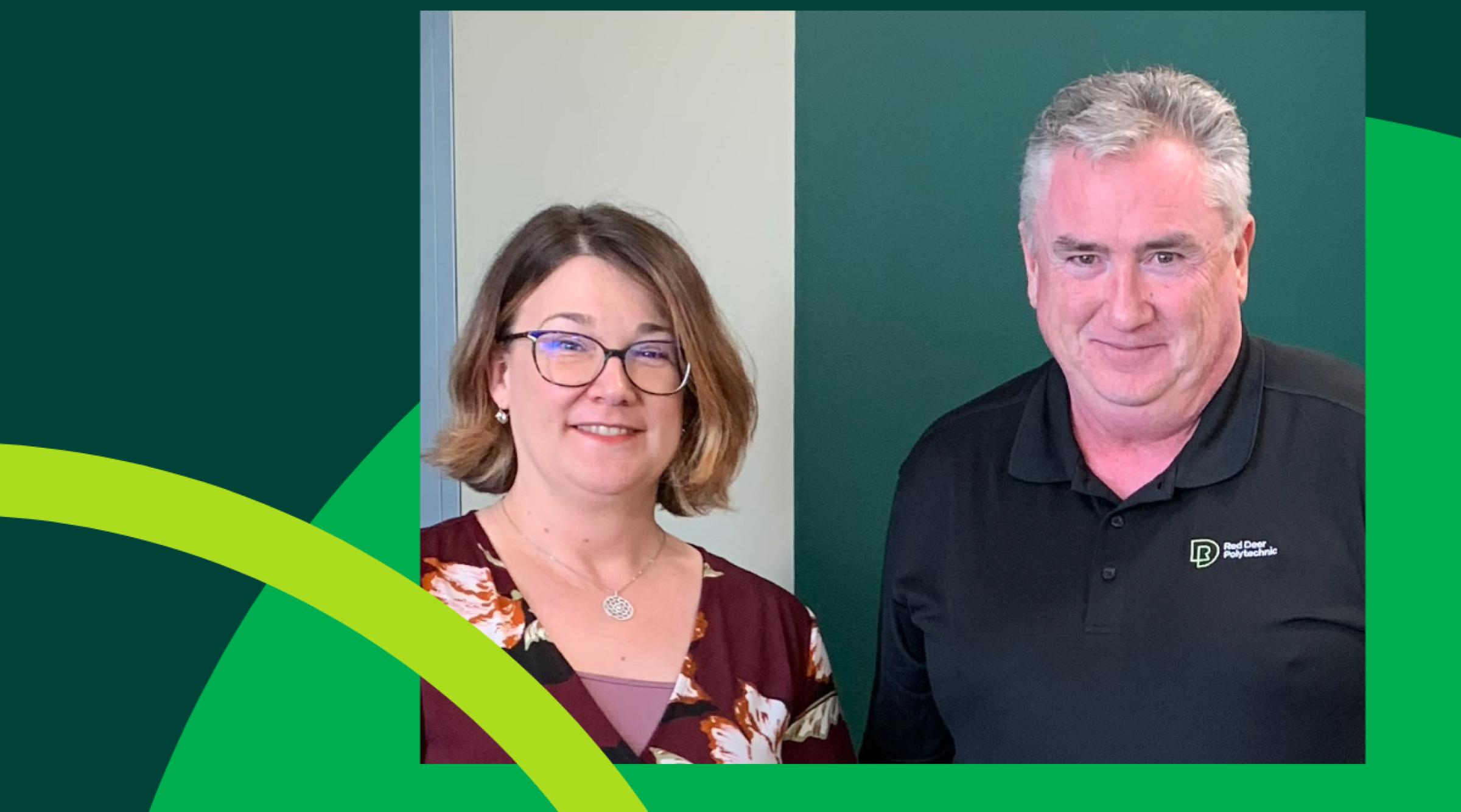 Alison Jeppesen and Raymond Savage stand beside each other against a green and white wall while smiling at the camera