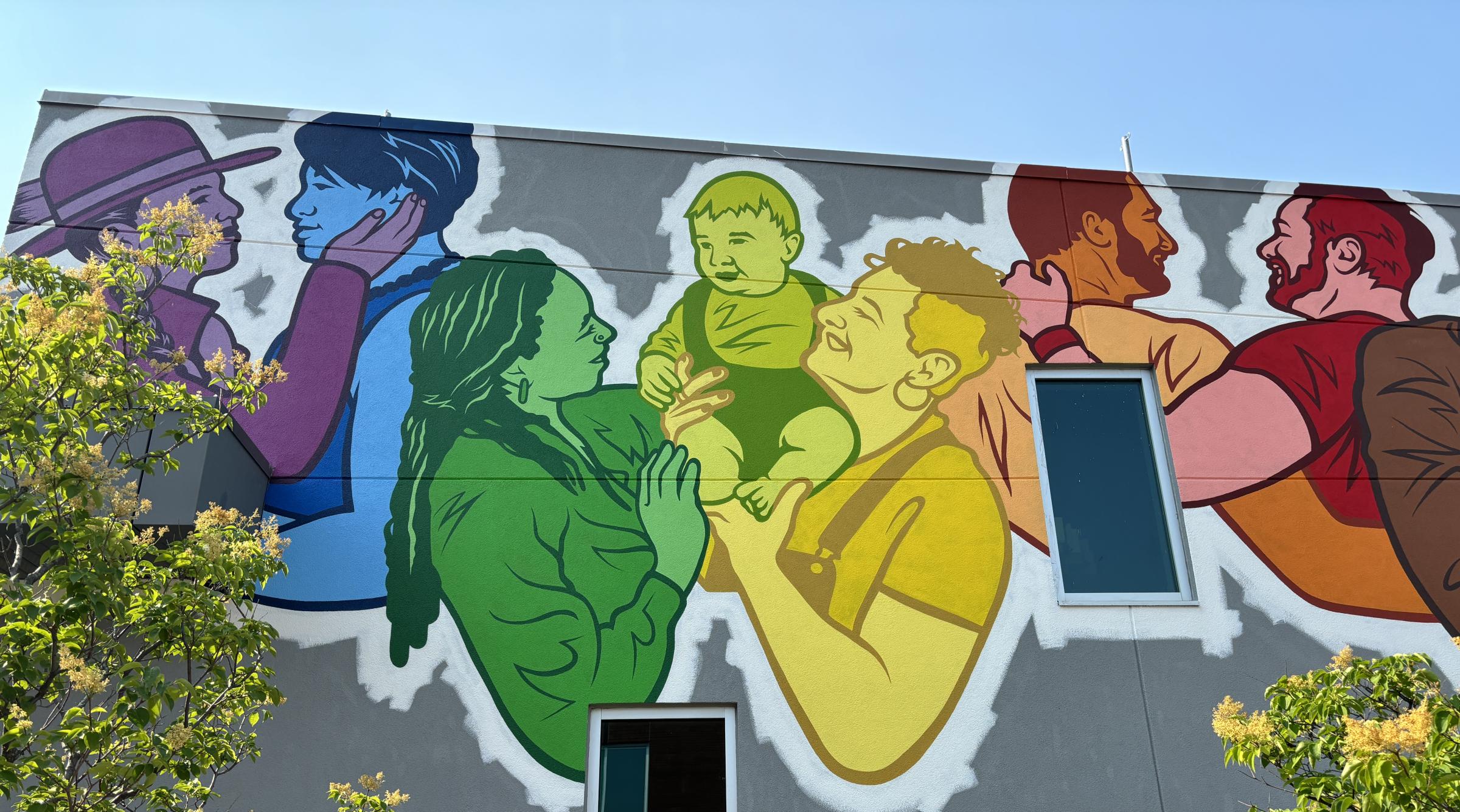 A partial photo of the new Pride mural. It features a diverse group of genders and races smiling and showing affection to each other in the Pride colours