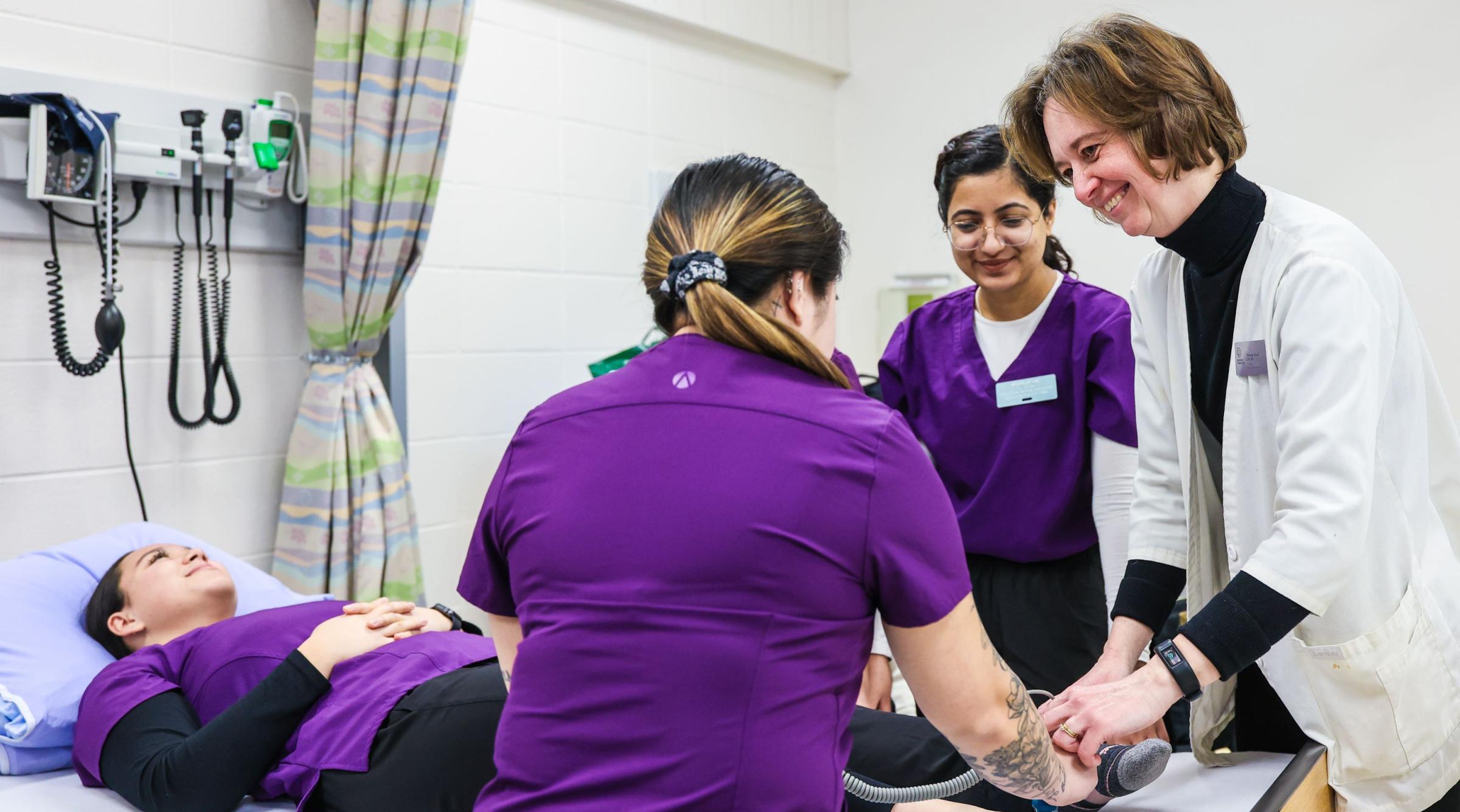 A group of student nurses and a faculty member practice their techniques on another student