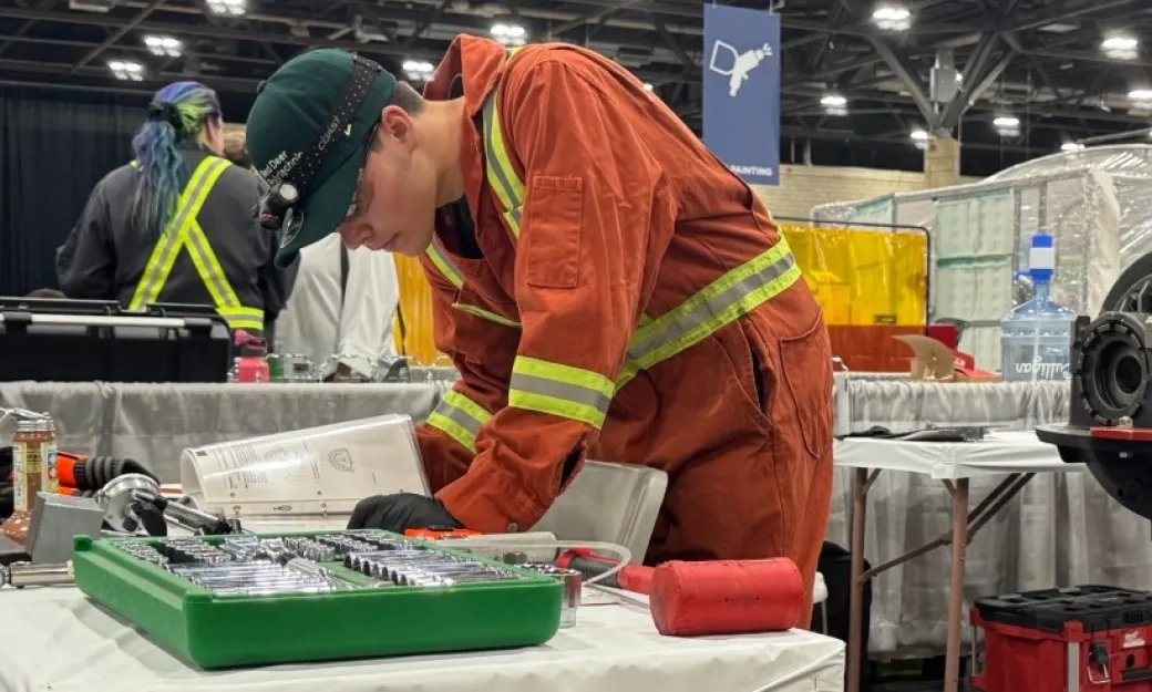Miles Alger wearing orange coveralls leans over some equipment at Skills Canada Alberta 2025