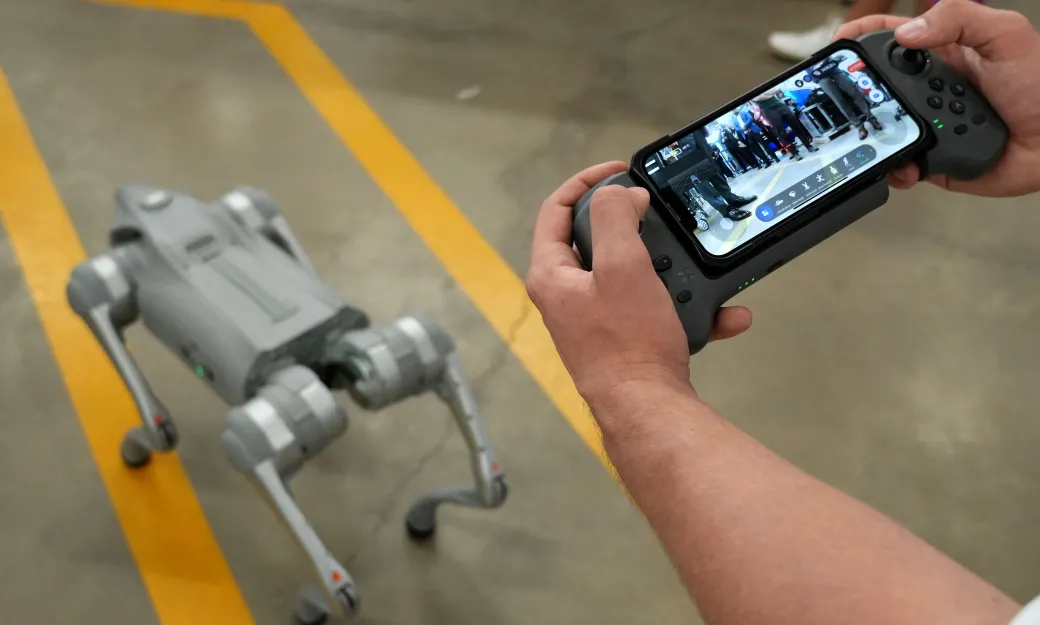Hands holding a controller for Dr. Woof, a robot dog, in the foreground and Dr. Woof in the background