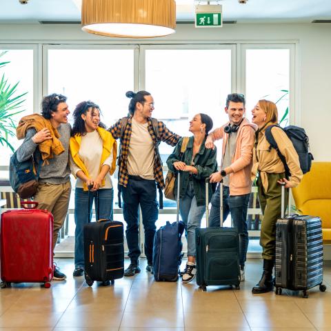 A group of travelers with luggage laughing together in front of large windows.