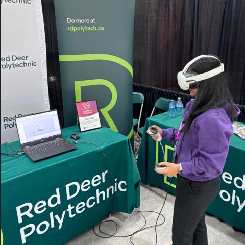 A woman wears a VR headset and holds controls in front of a RDP booth