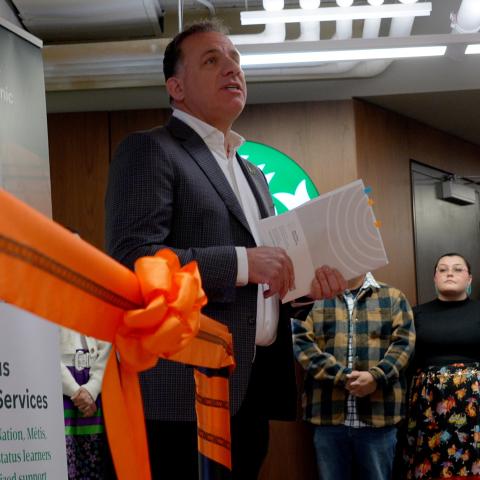 Stuart Cullum speaks in front of a large crowd with an orange ribbon in the foreground