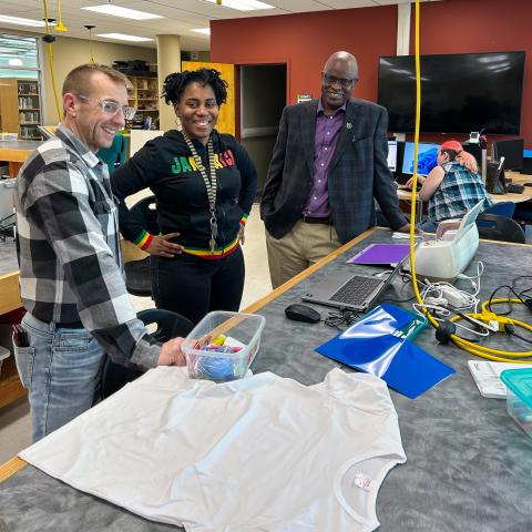 Three employees smile at the camera while standing at the tshirt making activity.