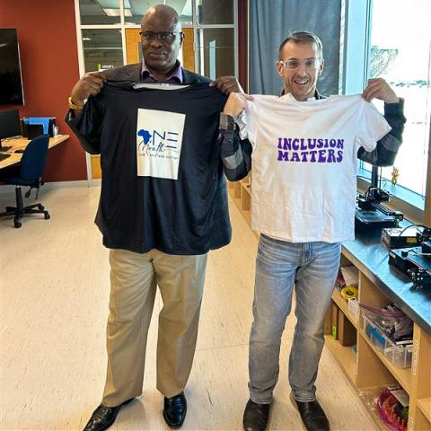 Two employees hold up the shirts they made.