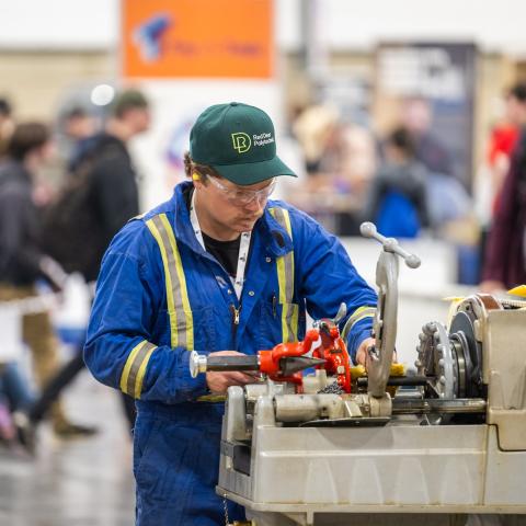 An RDP student in blue coveralls and an RDP hat operates a large piece of equipment at Skills Canada Alberta 2025