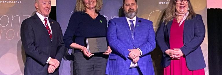 A smiling group of stands around Alicia Caffereta who holds her recent award