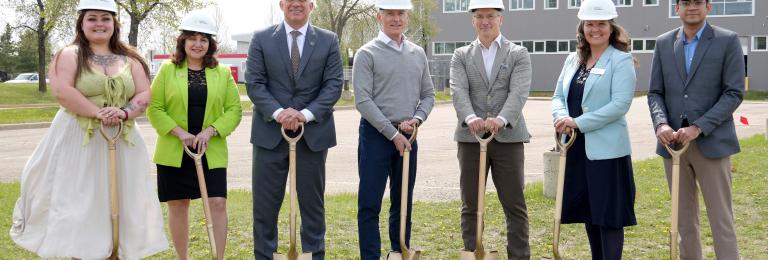 A group of RDP and Government of Alberta reps wear hardhats while holding shovels