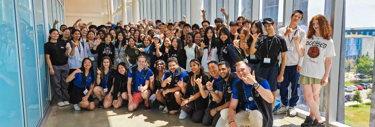 A large group of diverse high school students pose in a long corridor of windows