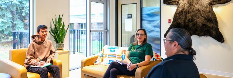 A group of three sit on comfortable looking couches at the Pónokaisissáhta Indigenous Student Centre