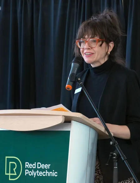 A female speaker stands behind an RDP podium at the Recovery On Campus event