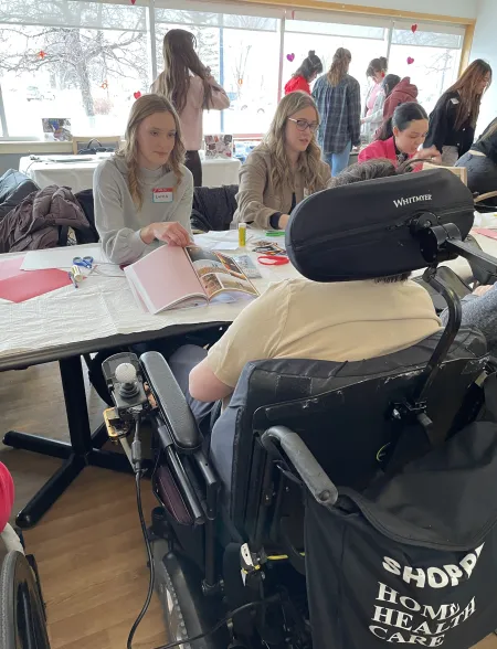 A group of students sit across from residents at Bethany Care Society while showing them various artbooks