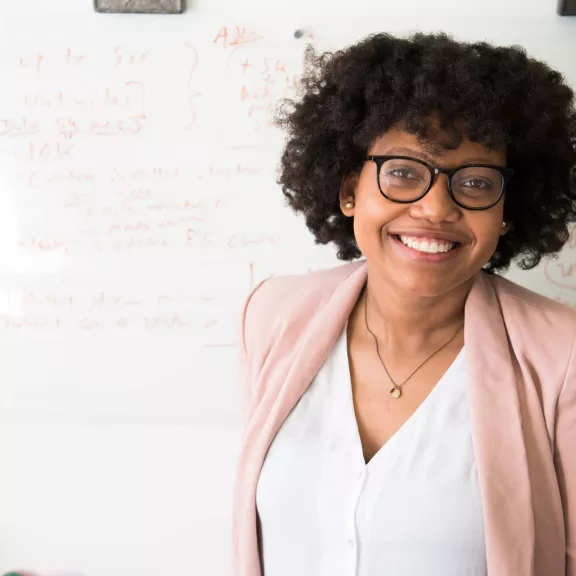 Woman looking at the camera with a whiteboard behind her.