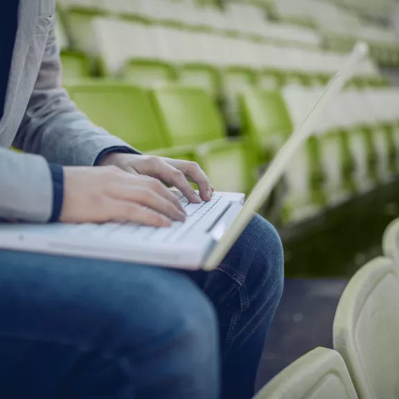 Person on a laptop seated in gymnasium seating.