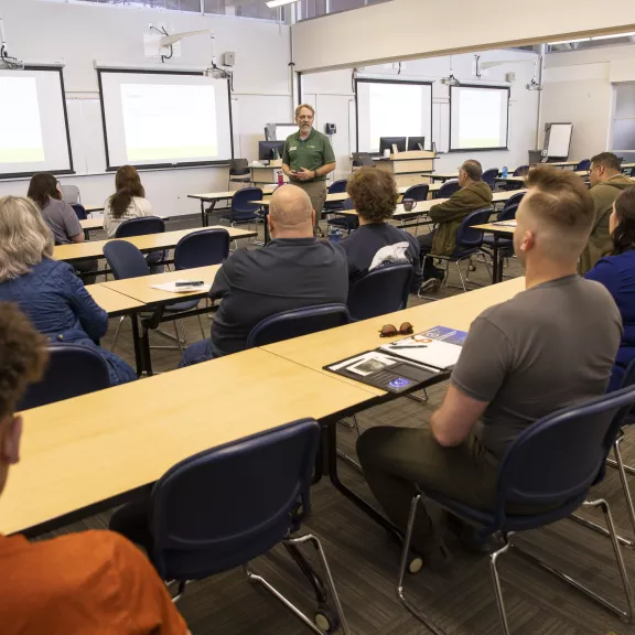 Instructor at the front of class leading a large cohort of mature students.
