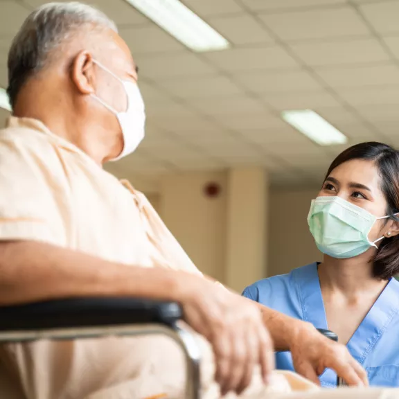 a nursing student in conversation with a patient in a wheelchair. both are masked.