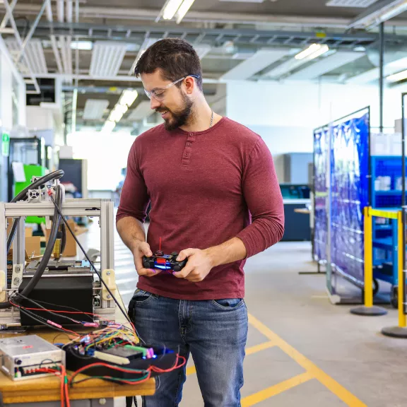 Student stands with a remote control looking at a table full of high-tech equipment