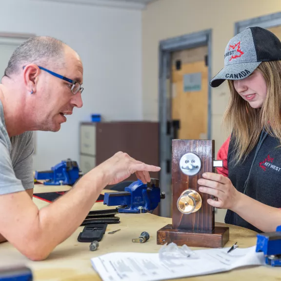 An instructor shows a student the inner workings of a door locking system.