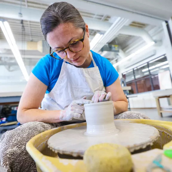 An artist shapes a vessel on a pottery wheel.