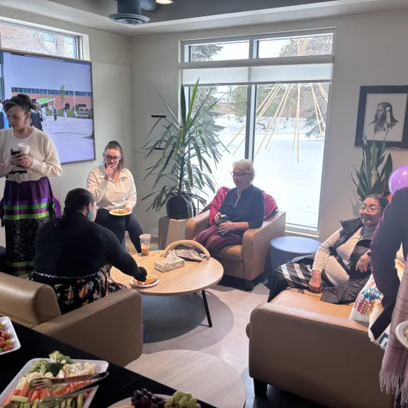 A group sits in front of a bright window inside the Pónokaisissáhta Indigenous Student Centre