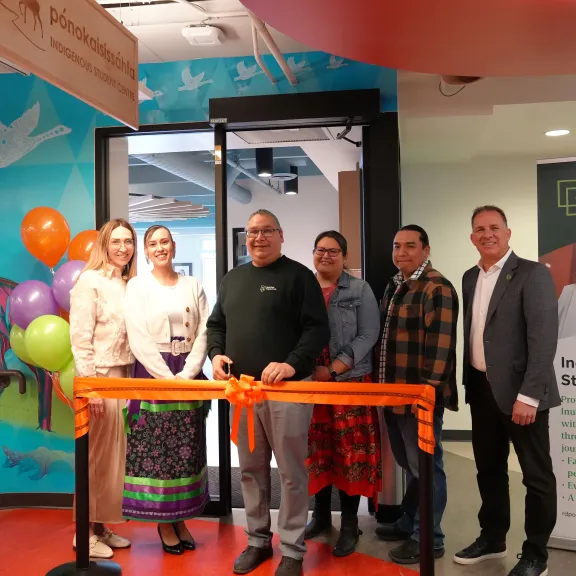 A group of RDP staff and students stand in front of an orange ribbon ready to cut it