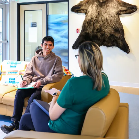 A smiling male Indigenous student sits smiling at a woman who sits across from him