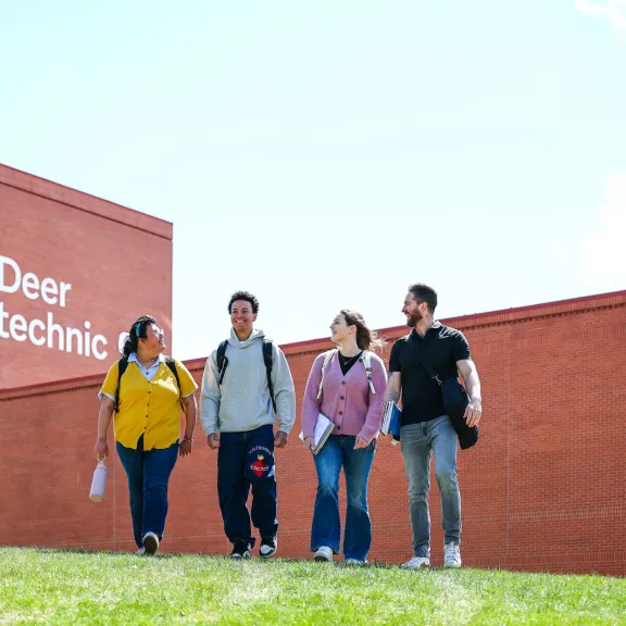 A group of four diverse students walk on a grassy hill outside the Arts Centre at RDP. The RDP name and logo are visible on the side of the building