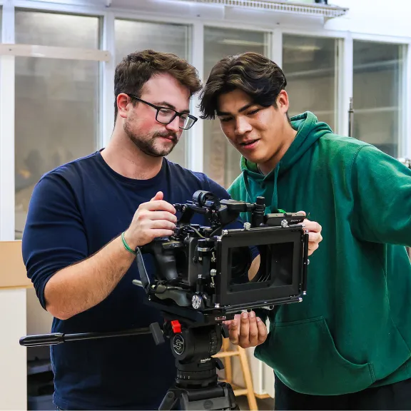 Two male students operate a large video camera