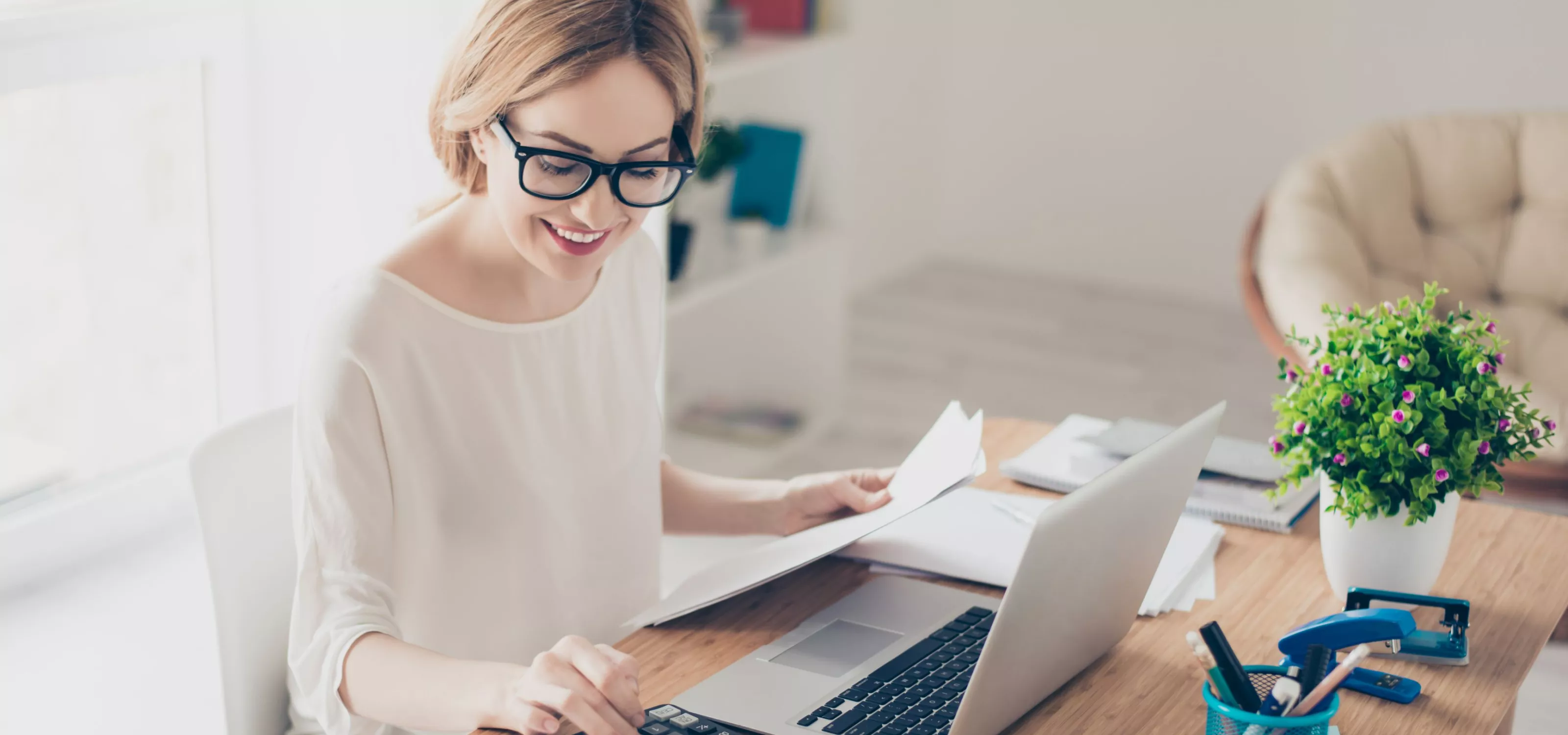 Woman with calculator and laptop performing bookkeeping tasks.