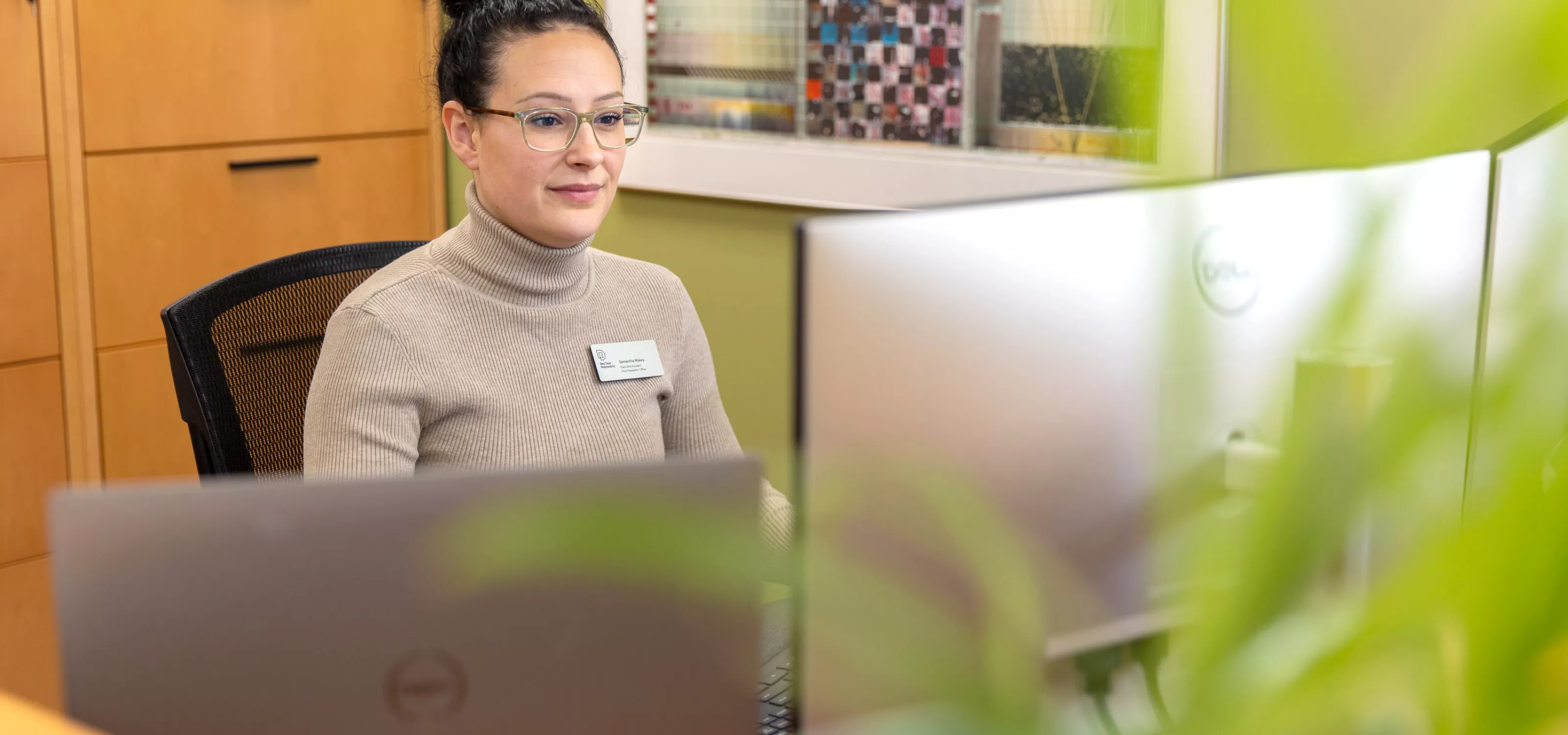 An executive assistant works at a desk with artwork & green plants surrounding her.