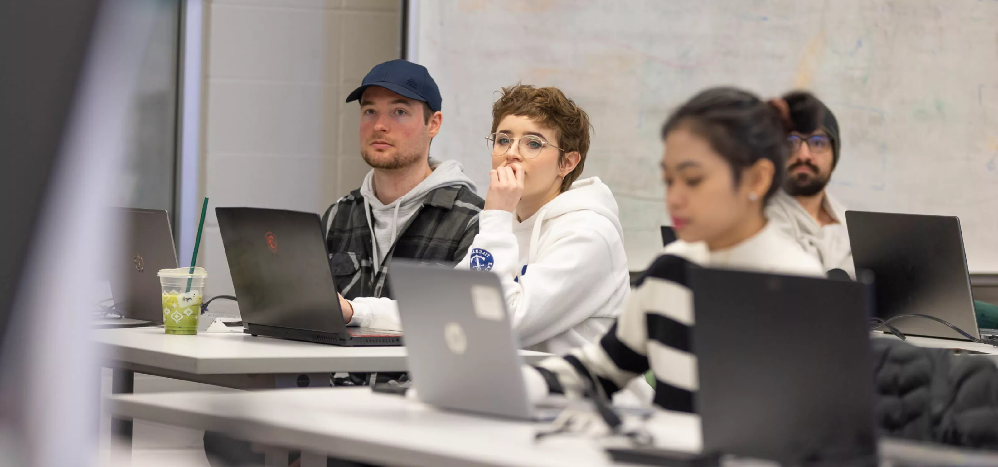 A group of three students on laptops look just off-camera looking very focused